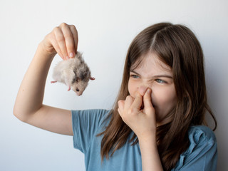 A little girl holds in her hand a hamster that smells bad